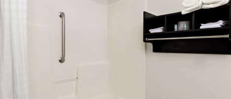 A bathroom with a shower, a grab bar, a towel rack with towels, and a shelf with toiletries.