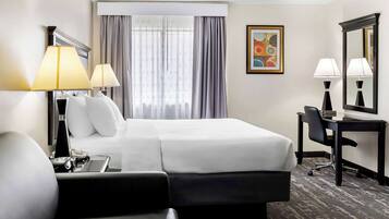 Habitación de hotel con cama, dos lámparas de noche, escritorio con silla, un espejo grande y ventana con cortinas.