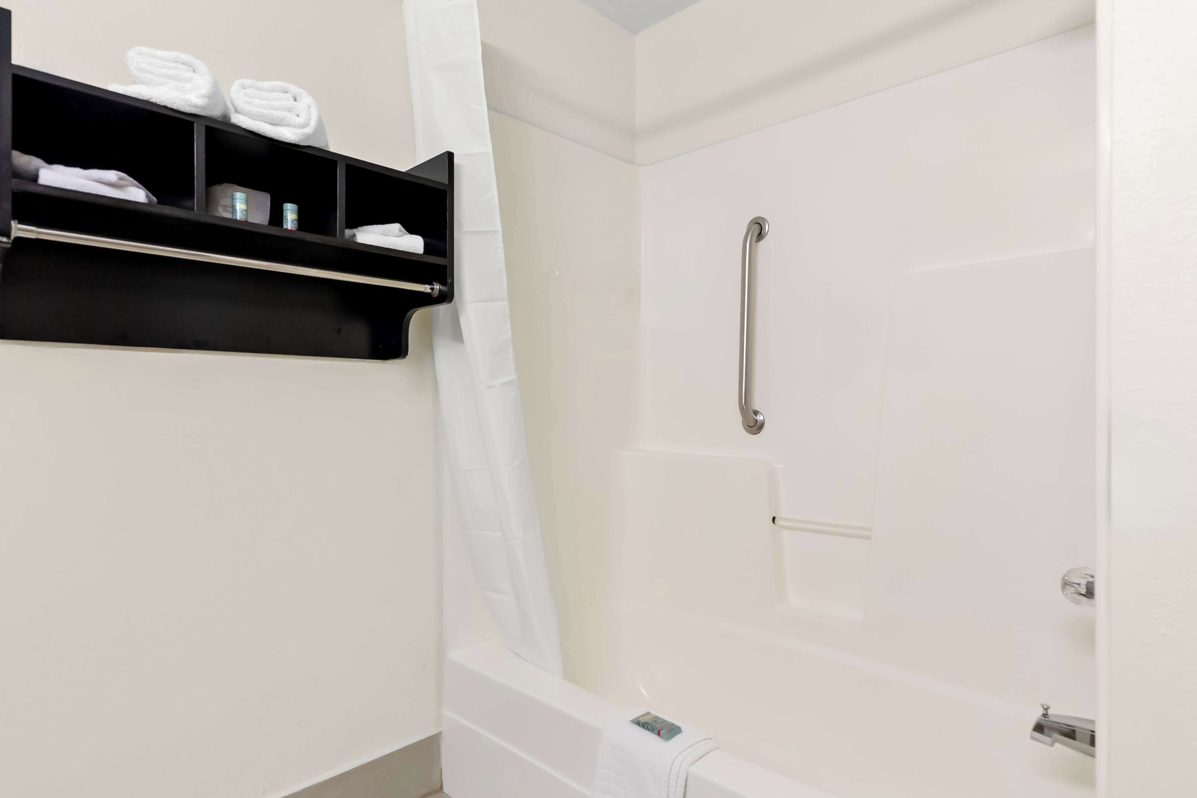 A bathroom with a white bathtub, a shower with a grab bar, and a shelf with towels and toiletries.