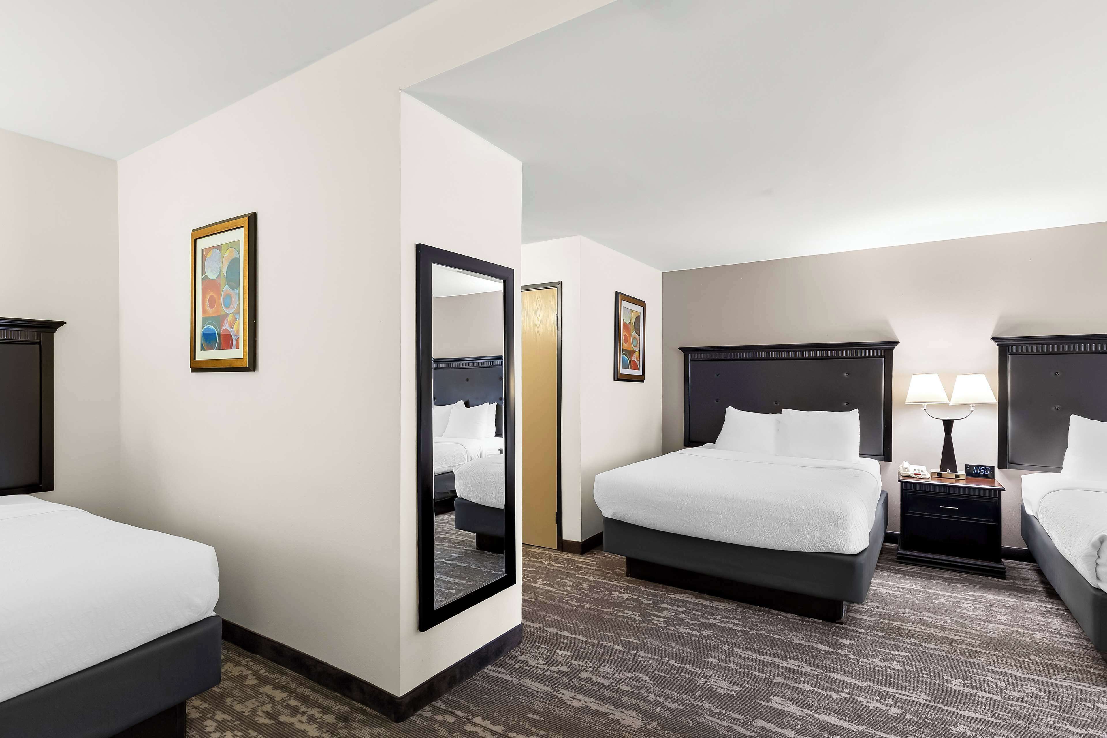 A hotel room with two beds, a large mirror, and a nightstand with a lamp.