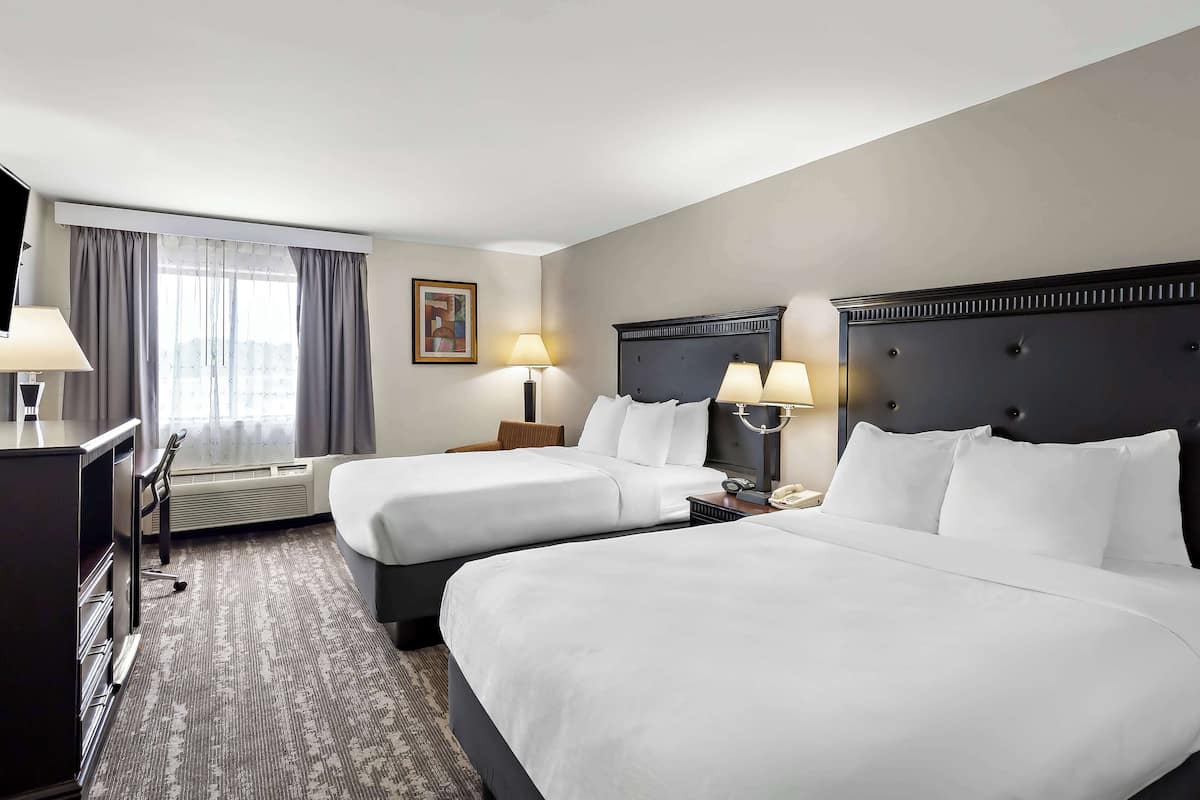 A hotel room with two beds, a desk, and a chair.