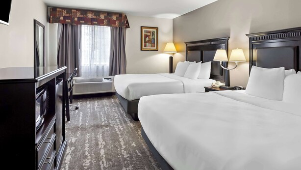 Une chambre d’hôtel avec deux lits, un bureau, une chaise, une télévision, une lampe et un tableau au mur.