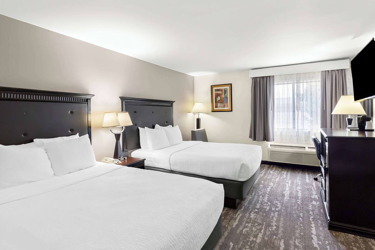 A hotel room with two beds, a desk, a chair, a TV, and a window with curtains.