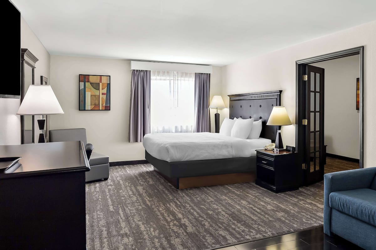 A hotel room with a bed, bedside tables, a desk, a chair, and a large window with curtains.