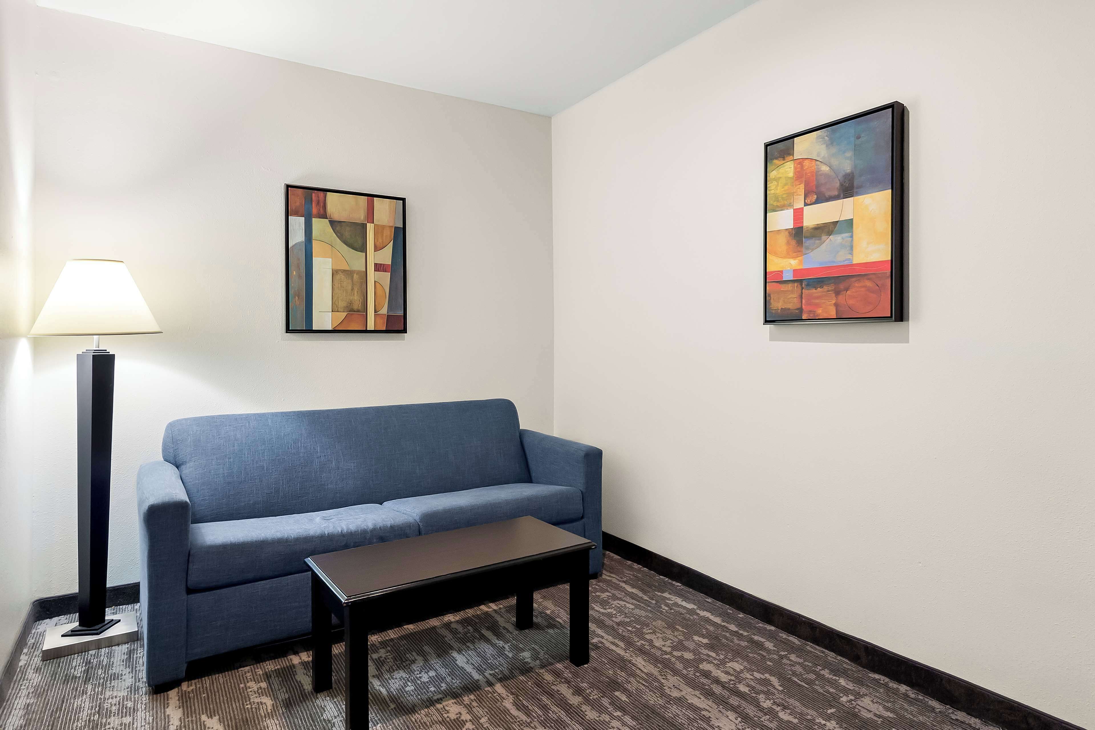 A room with a blue sofa, a small table, a lamp, and two abstract paintings on the walls.