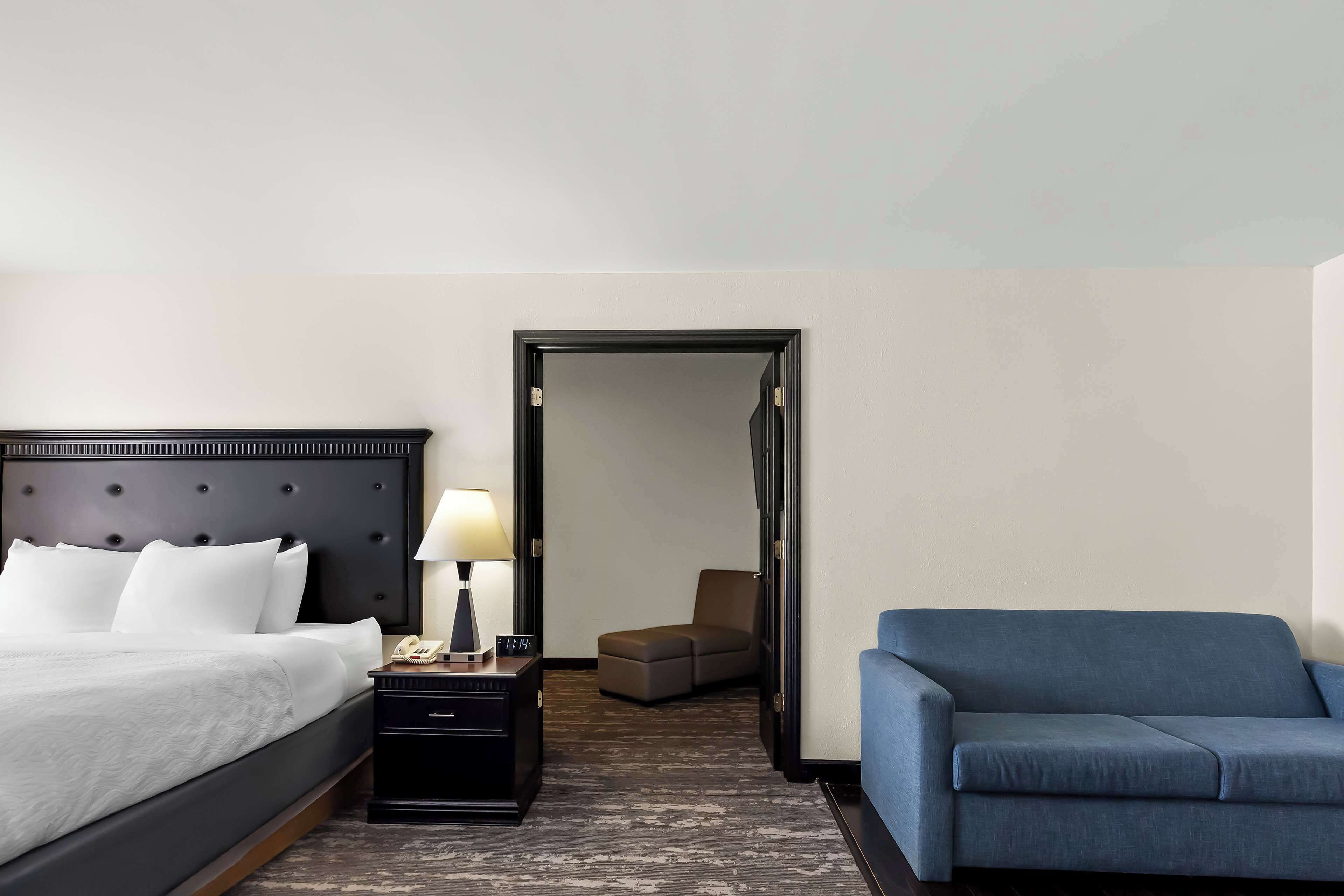 Habitación de hotel con cama, mesita de noche con lámpara, sofá azul y puerta que da a otra habitación.