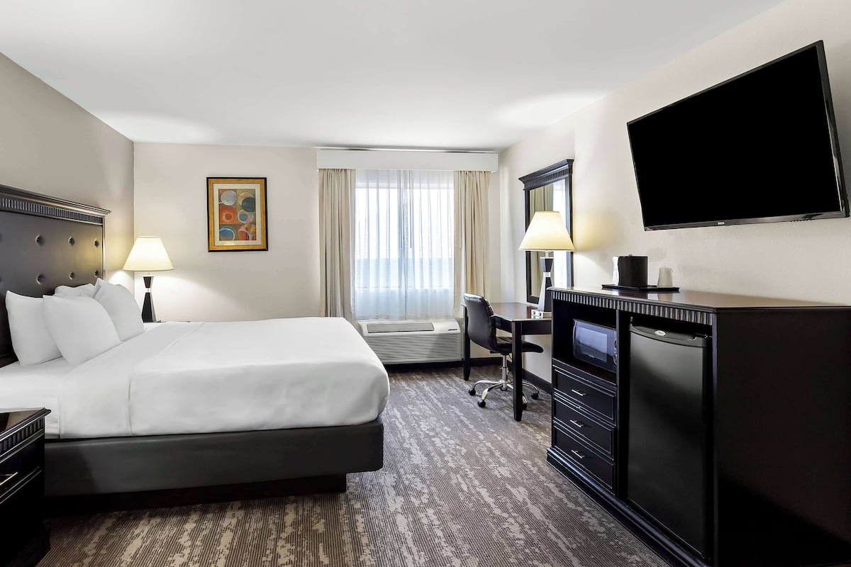 A hotel room with a large bed, a desk, a flat-screen TV, a dresser, and a window with curtains.