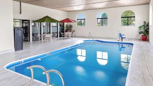 Une piscine intérieure à l’eau d’un bleu limpide, dotée d’un parasol et d’un espace détente avec des chaises et une table.