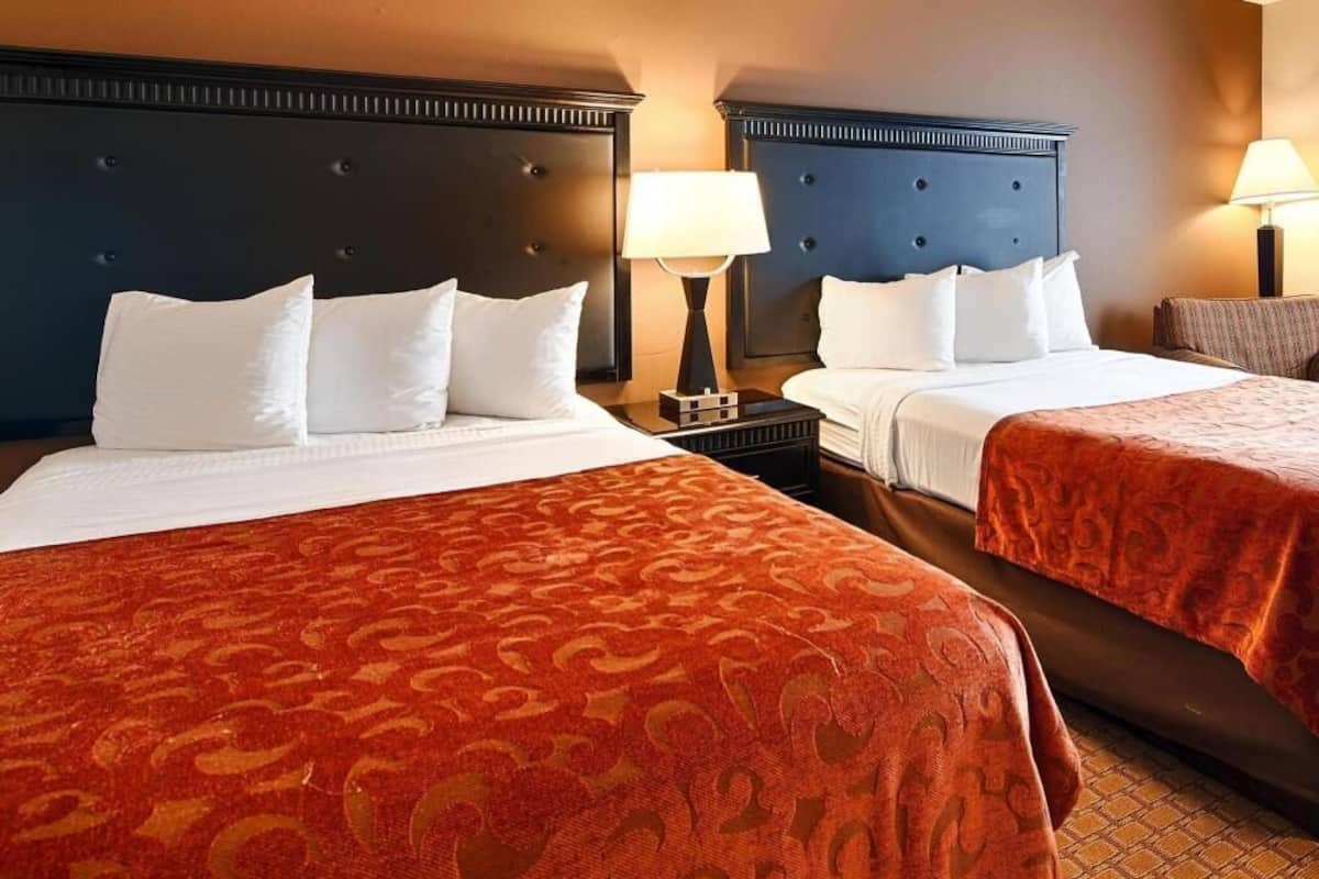 A hotel room with two beds, each with a headboard, a nightstand with a lamp, and a patterned bedspread.