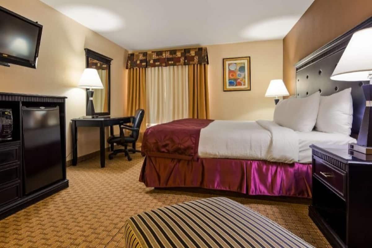 A hotel room with a bed, desk, chair, television, and a small table.
