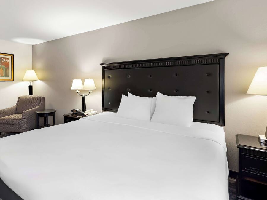 Habitación de hotel con una cama grande, dos mesitas de noche con lámparas, una silla e imagen enmarcada en la pared.