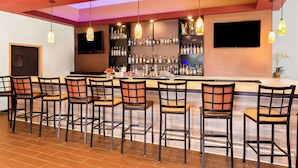 Un espace bar doté de plusieurs tabourets, d’un comptoir, d’étagères remplies de bouteilles d’alcool et de luminaires suspendus.