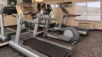A gym with treadmills, ellipticals, and stationary bikes, equipped with digital displays and mirrors.