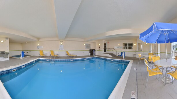 Une piscine intérieure avec des chaises et des tables jaunes, une bouée de sauvetage et des panneaux d’indication des sorties.