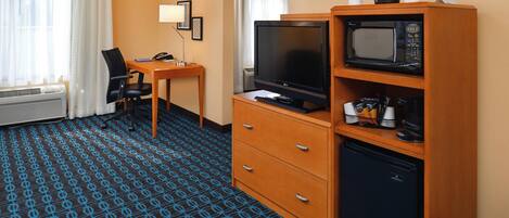 A hotel room with a desk, chair, television, microwave, and a small refrigerator.