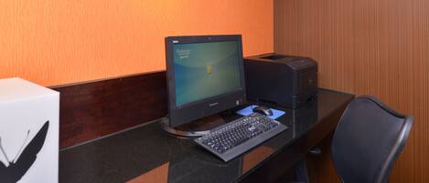 A computer desk with a monitor, keyboard, and printer in a room with a wooden wall and a sign that reads "Connect & Print".