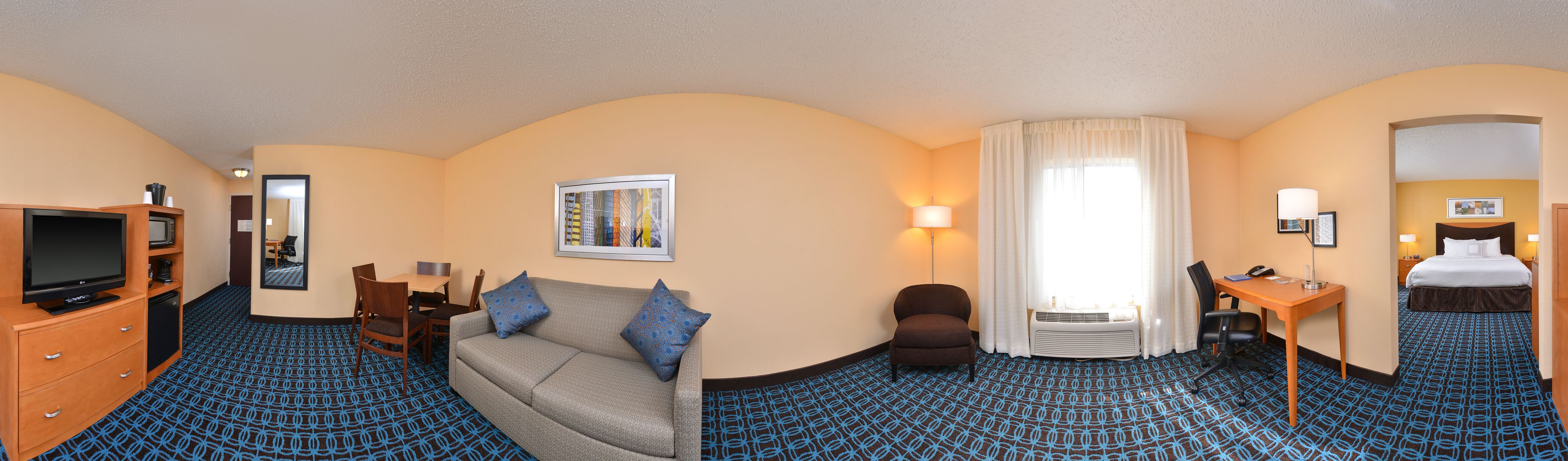 A hotel room with a sofa, a TV, a desk, a chair, and a bed.