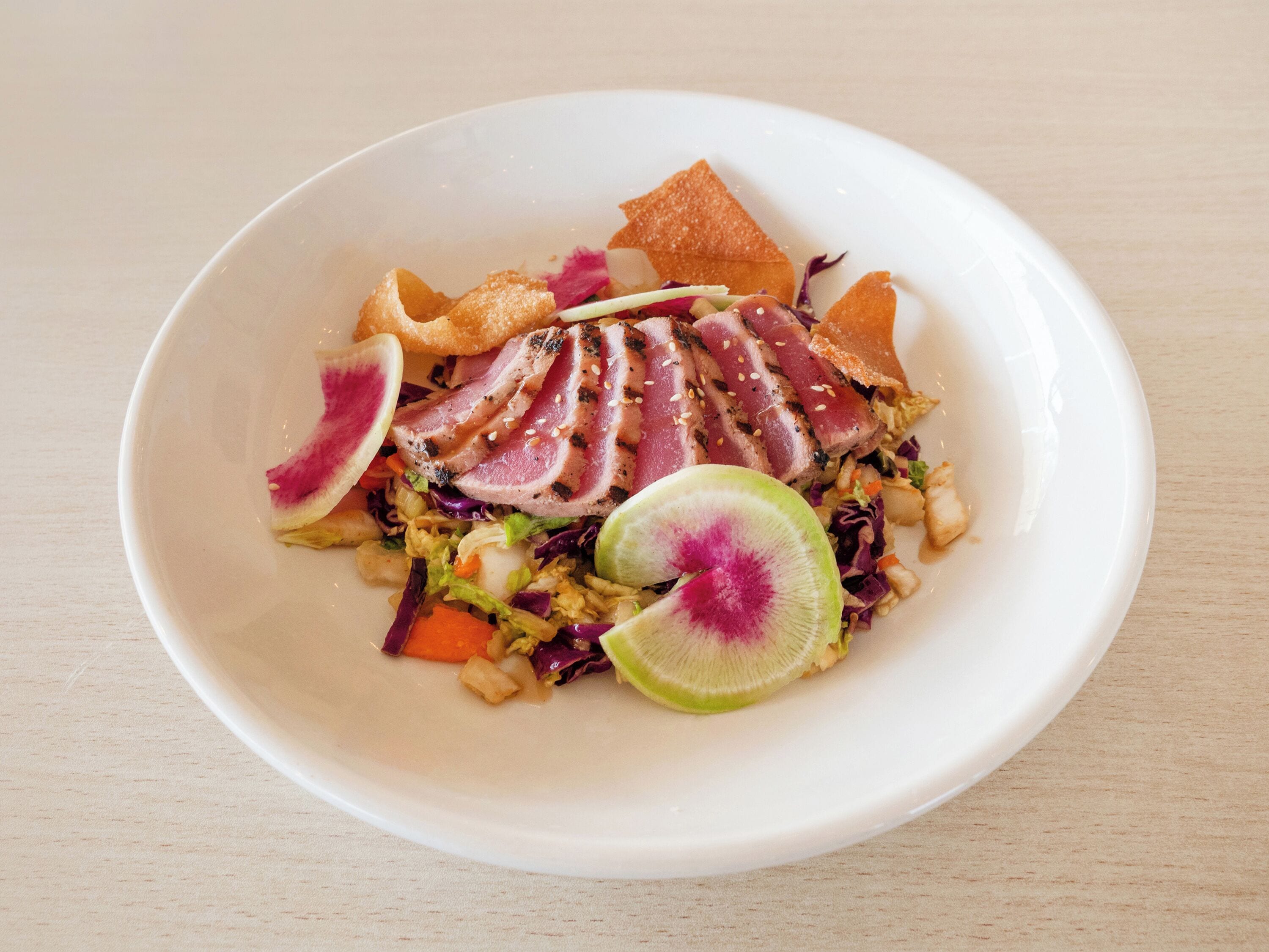 A white bowl containing a salad with sliced meat, vegetables, and a lime wedge.