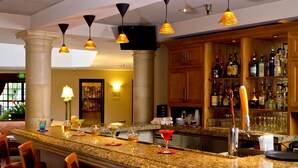A bar area with granite countertops, bar stools, and a variety of liquor bottles. - Coast Burbank Hotel (Burbank)