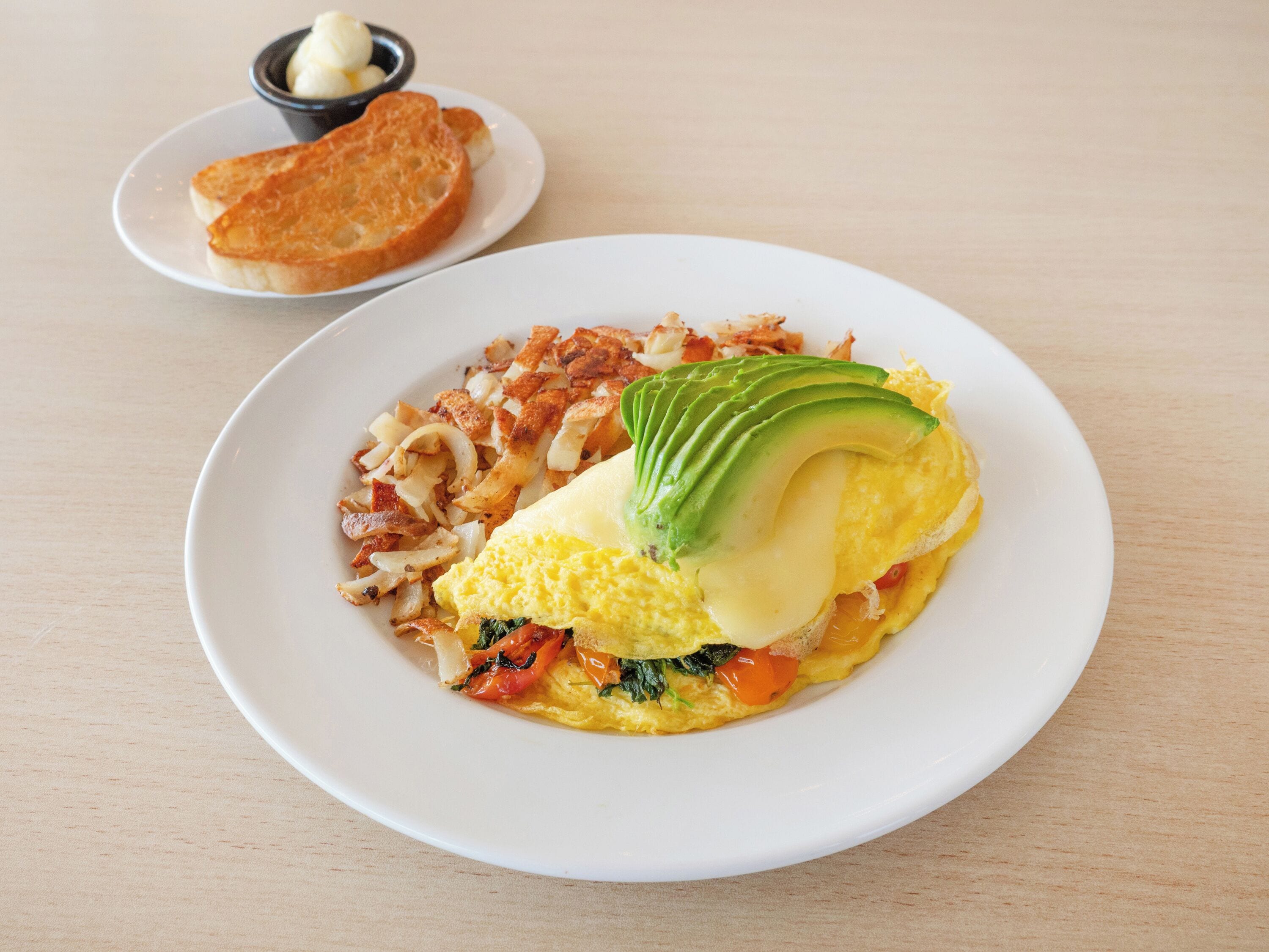 Une assiette contenant une omelette, de l’avocat et des légumes.