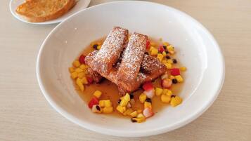 A plate of French toast with fruit and powdered sugar, accompanied by a small bowl of ice cream and a bowl of fruit.