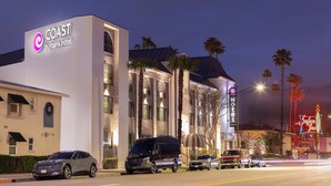 A hotel with a modern facade, palm trees, and a neon sign for a nearby establishment. - Coast Burbank Hotel (Burbank)