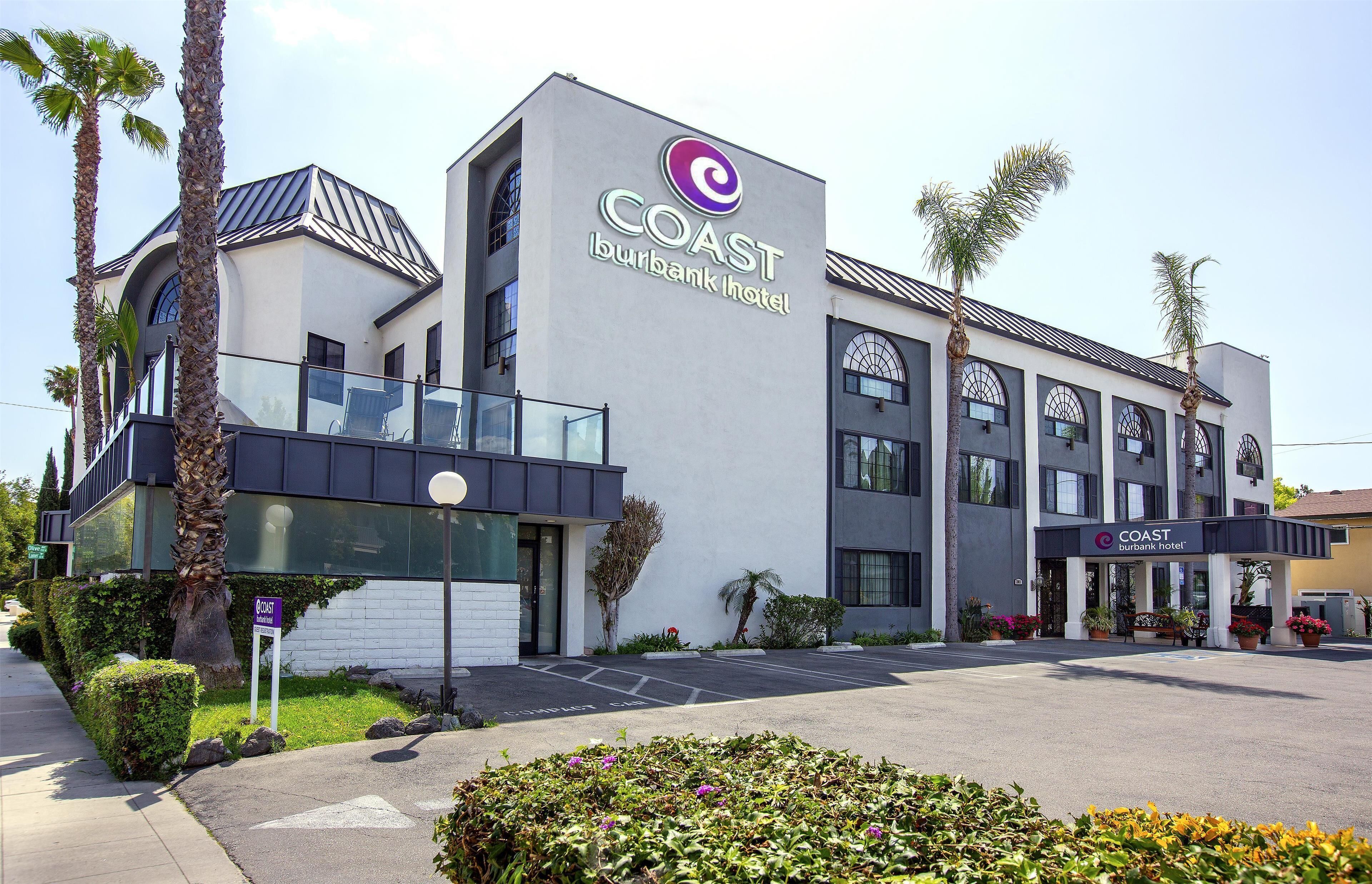 Um hotel moderno com um logotipo em destaque, entrada coberta e área de estacionamento.