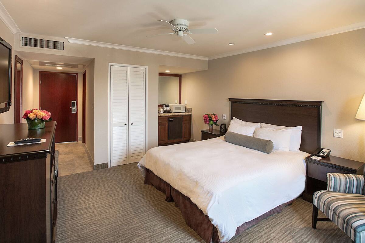 A hotel room with a bed, a desk, a chair, a microwave, and a ceiling fan.