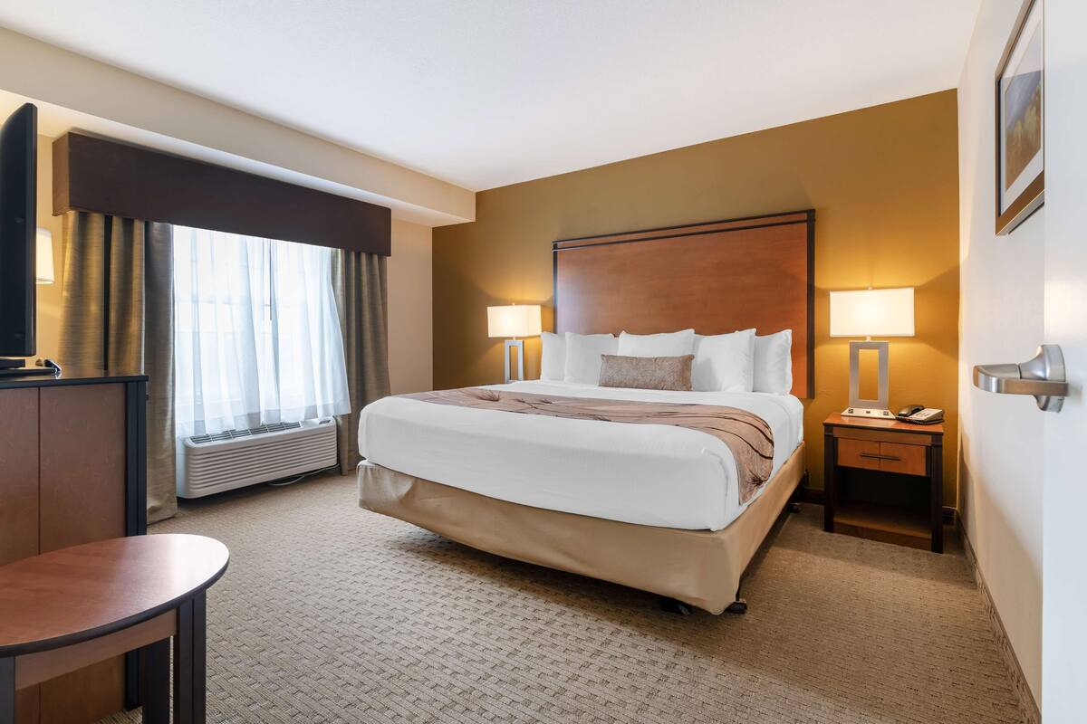 A hotel room with a large bed, two bedside tables with lamps, a desk, and a chair.