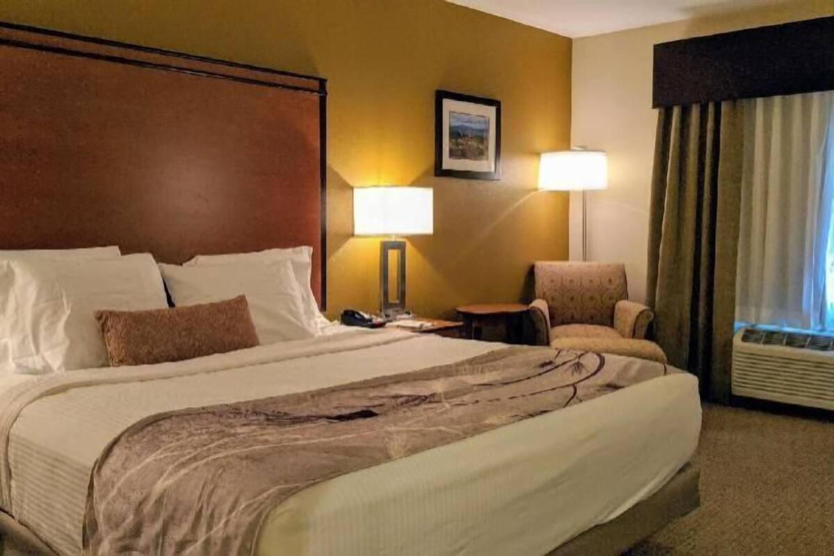 A hotel room with a large bed, two bedside lamps, a chair, a nightstand, and a window with curtains.