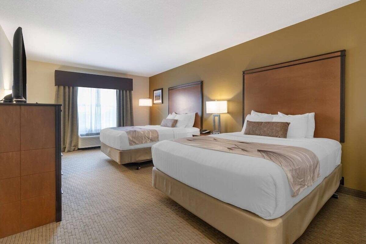 A hotel room with two beds, a television, and a large window with curtains.