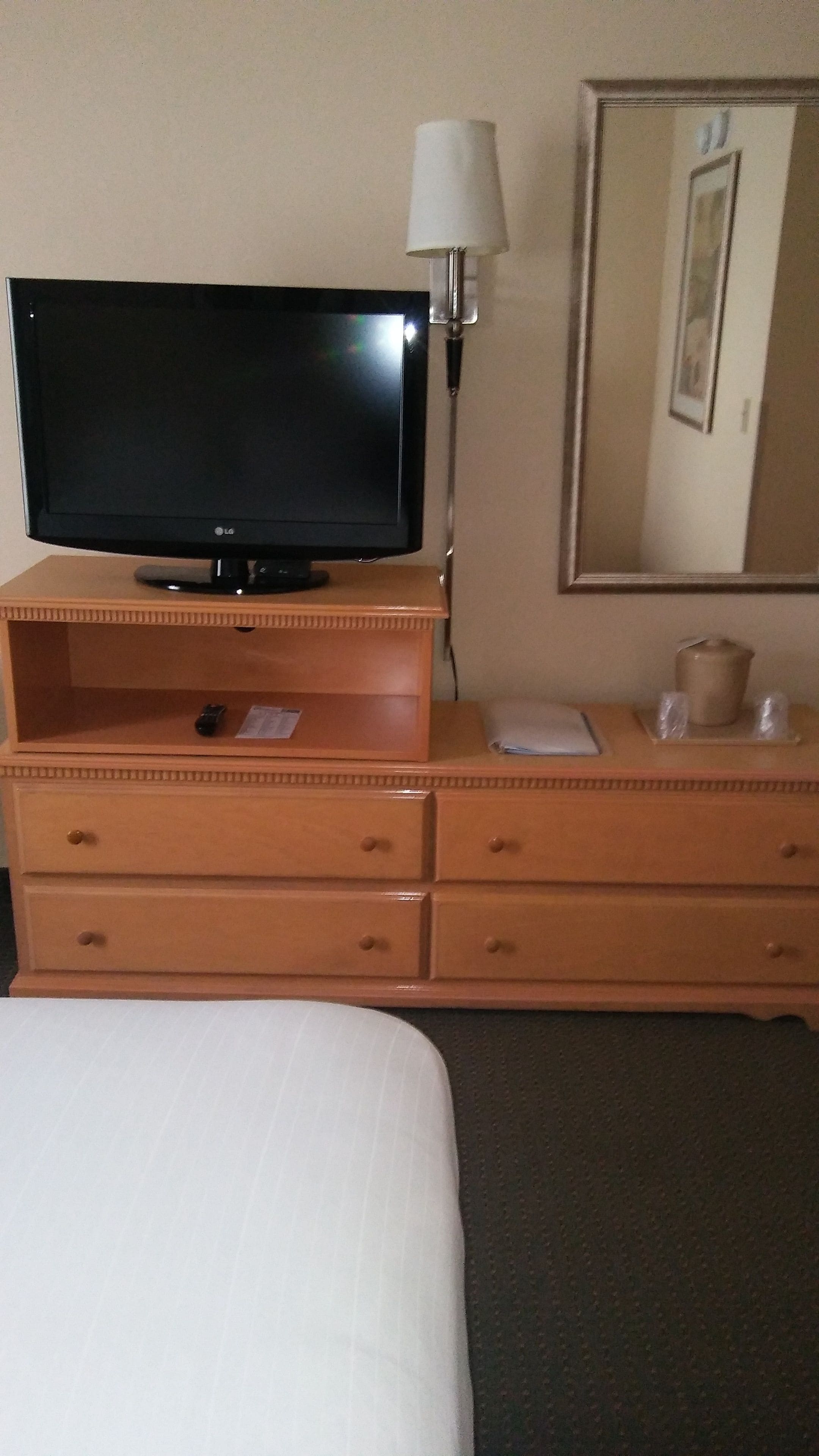 Une chambre d’hôtel avec un lit, une commode en bois, un téléviseur à écran plat, une lampe et un miroir.