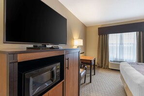 A hotel room with a flat-screen TV, a microwave, a dining table with chairs, a bed, and a large window with curtains.