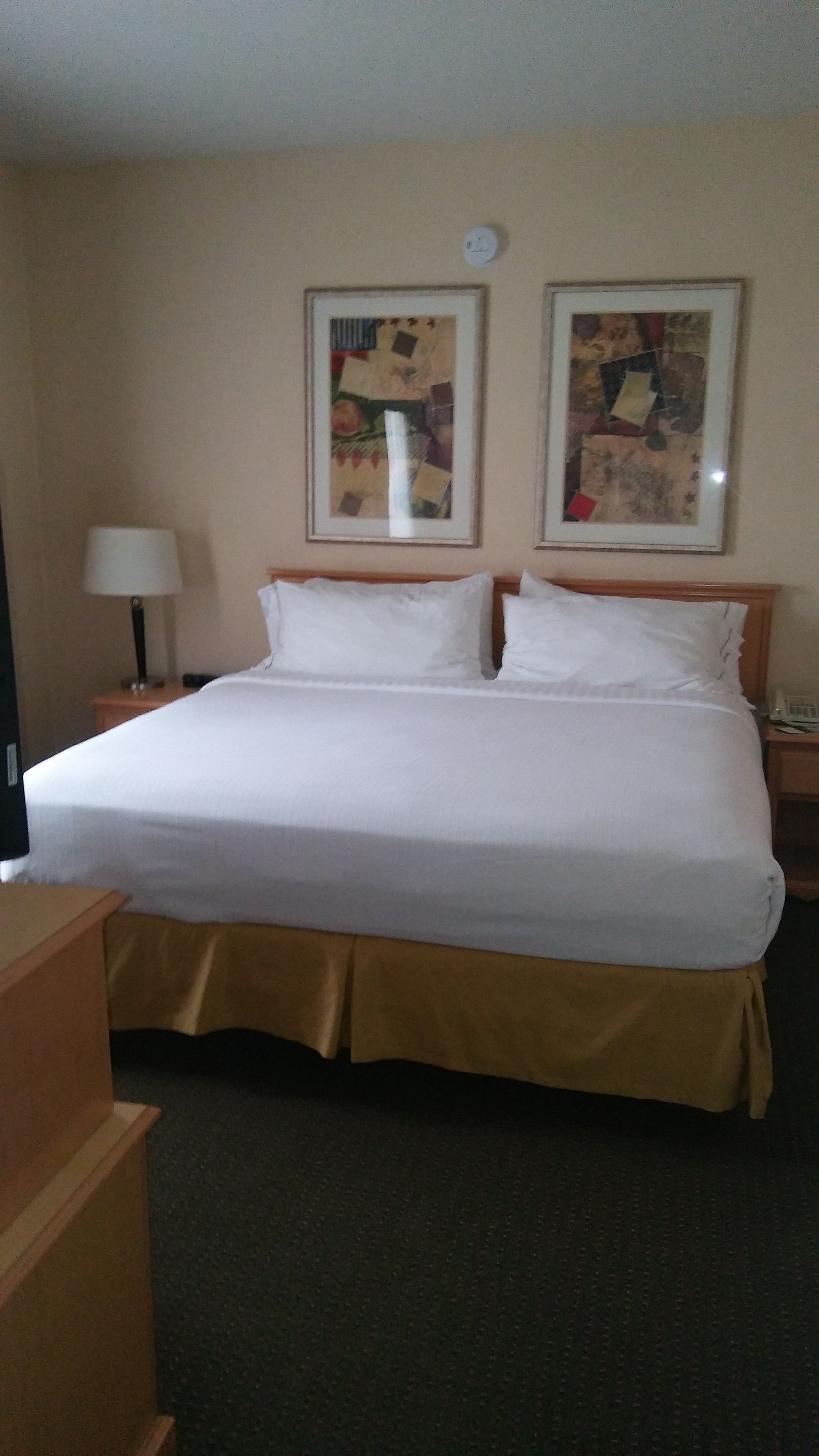A hotel room with a large bed, two bedside tables, a lamp, and two framed artworks on the wall.