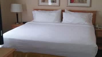 A hotel room with a large bed, two bedside tables, a lamp, and two framed artworks on the wall.
