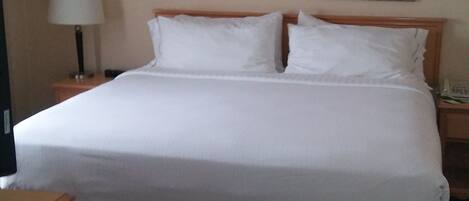 Una habitación de hotel con una cama grande, dos mesitas de noche, una lámpara y dos cuadros enmarcados en la pared.
