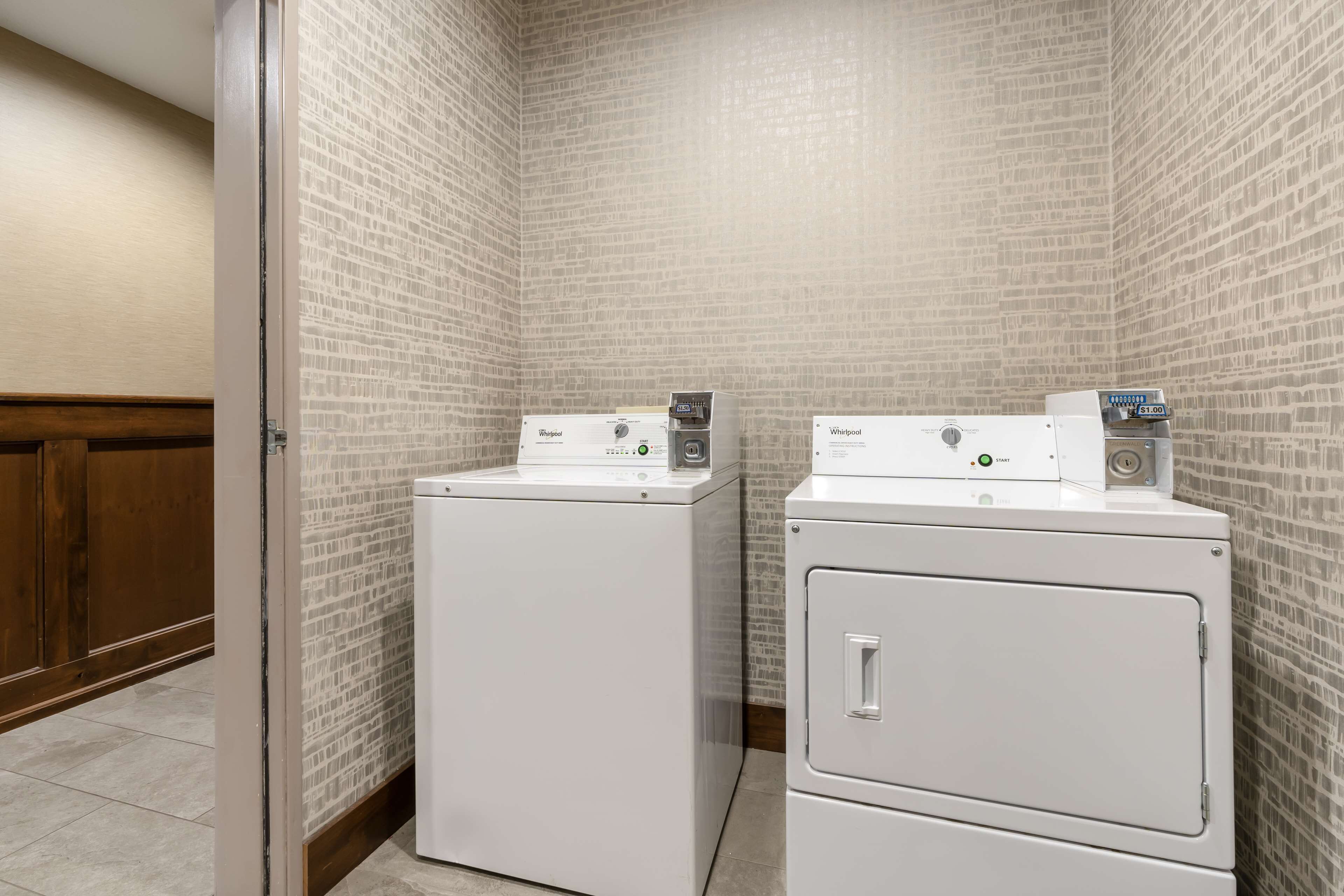 A laundry room with two stacked washers and dryers, a wooden door, and a brick-patterned wall.