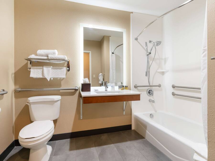 A bathroom with a toilet, sink, and bathtub. There are handrails and a mirror above the sink.