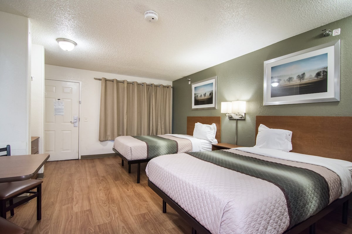 A hotel room with two beds, a desk, and a door.