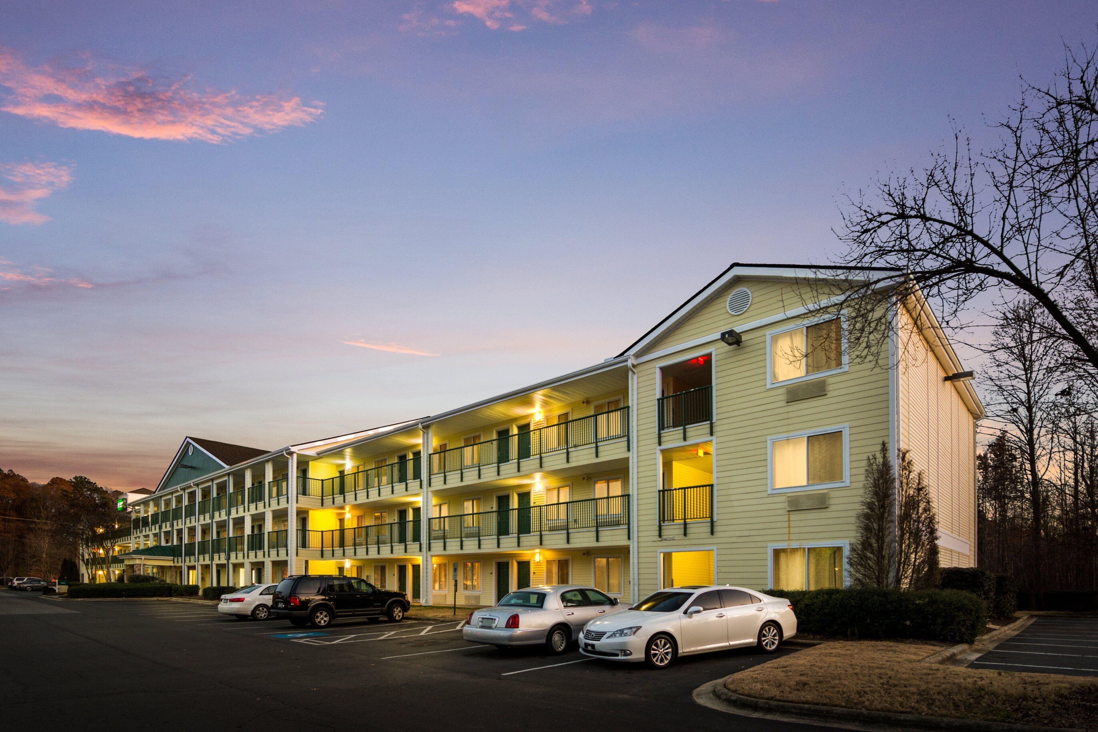 A multi-story hotel with a parking lot and several cars parked in front.