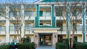 A multi-story hotel with a green and beige color scheme, a central entrance with a stone facade, and a mailbox. - Suburban Studios Durham-Raleigh (Durham)