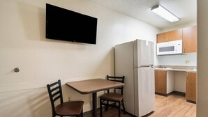 A compact kitchen with a refrigerator, microwave, and a flat-screen TV mounted on the wall. - Suburban Studios Durham-Raleigh (Durham)