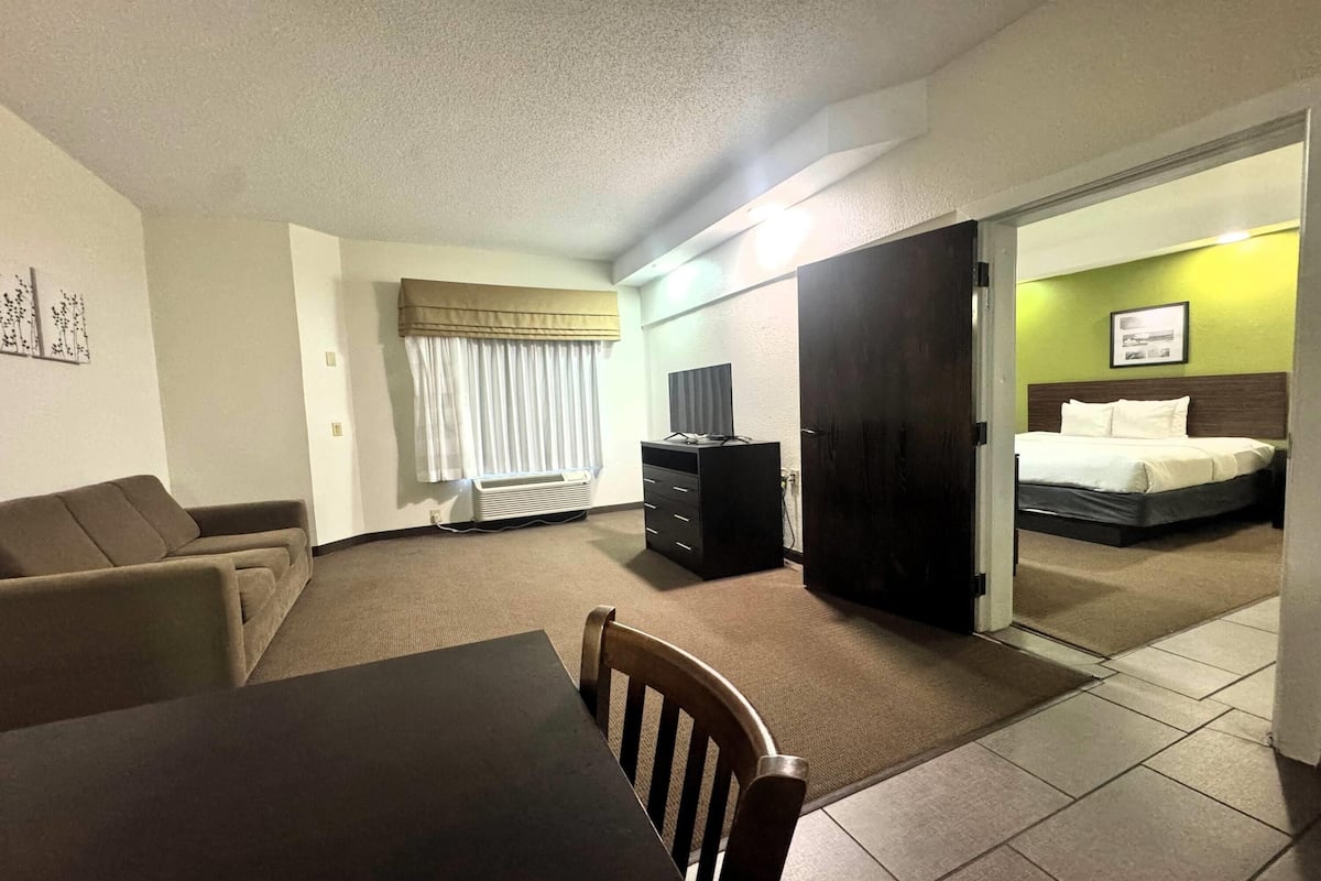 A hotel room with a dining area, a bed, a TV, and a desk.