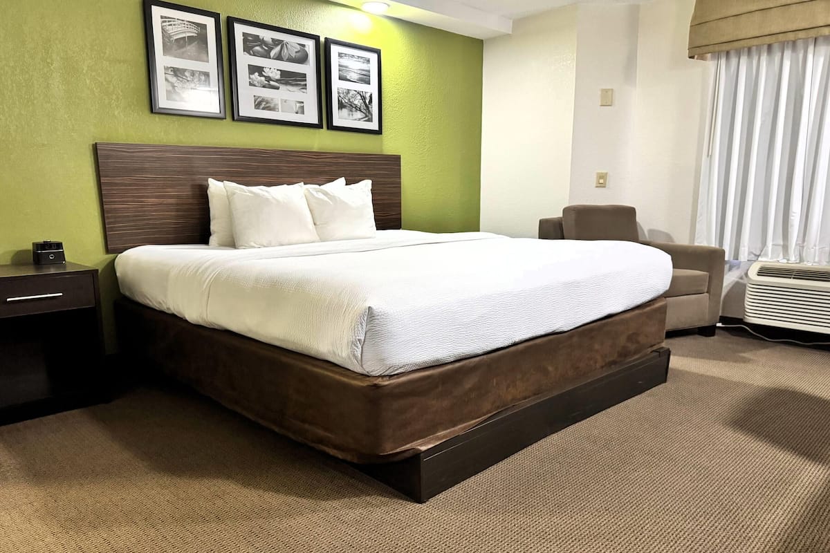 A hotel room with a large bed, a nightstand, a chair, and a window with curtains.