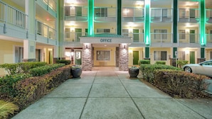 Un hotel de varios pisos con una entrada central marcada 'OFFICE', que presenta una fachada de piedra e iluminación exterior verde.