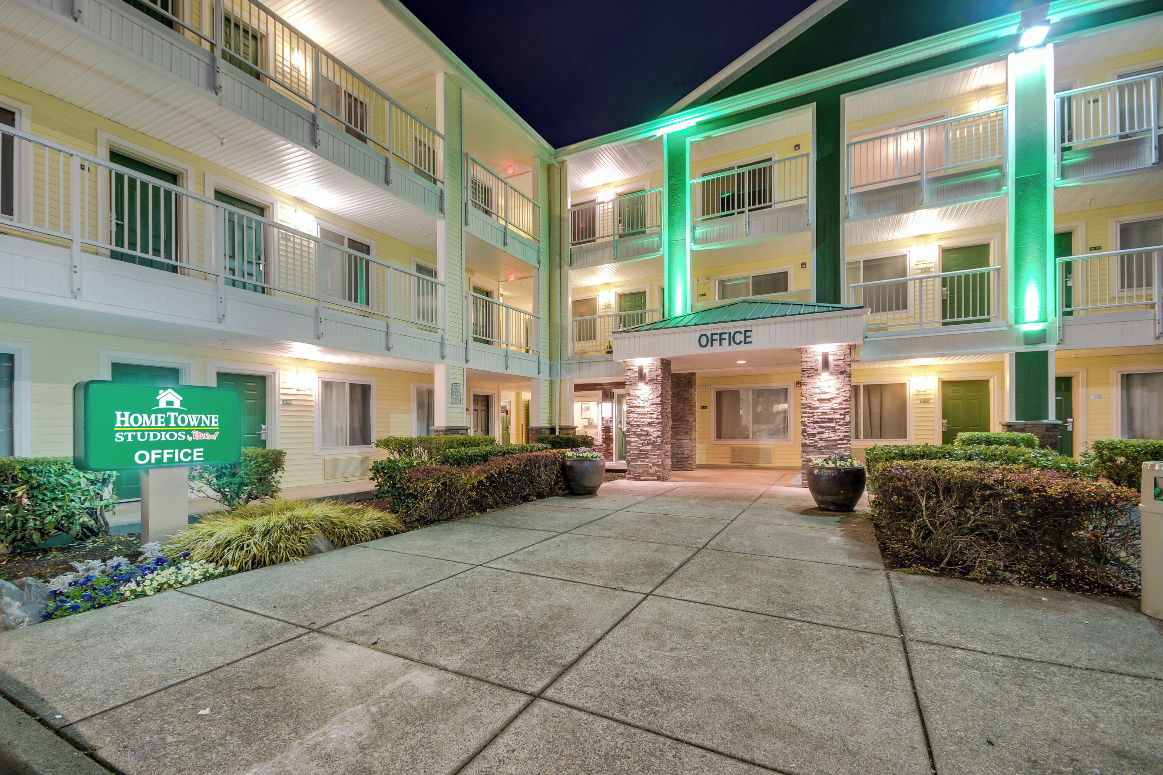 A multi-story hotel with a central courtyard, featuring a sign for the office and a green-lit entrance.