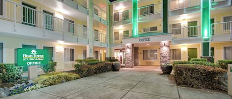 A multi-story hotel with a central courtyard, featuring a sign for the office and a green-lit entrance.