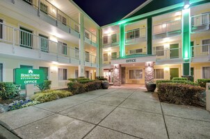 Un hotel de varios pisos con un patio central, que muestra un letrero para la oficina y una entrada iluminada en verde.