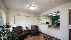 Un área de recepción con mostrador, dos sillones de cuero, una mesita con una planta, un cuadro en la pared y una pared verde con el letrero 'HOME STUDIO'.