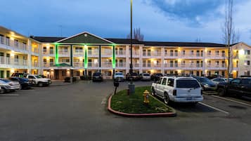 Un motel de varios pisos con una oficina central, múltiples balcones y un estacionamiento con varios vehículos.